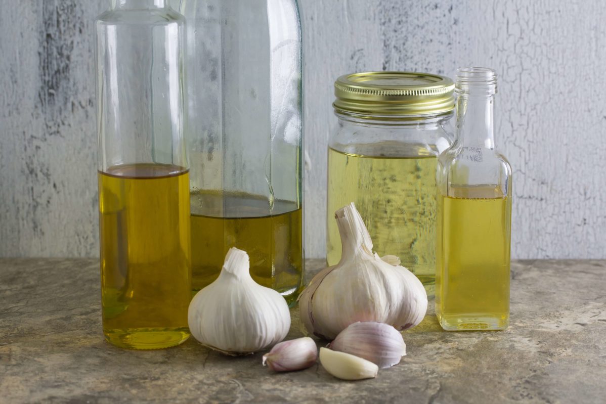 Plump and firm garlic clove heads in front of bottles of garlic infused oil. Monash University Certified Low FODMAP Recipe for Garlic-Infused Oil