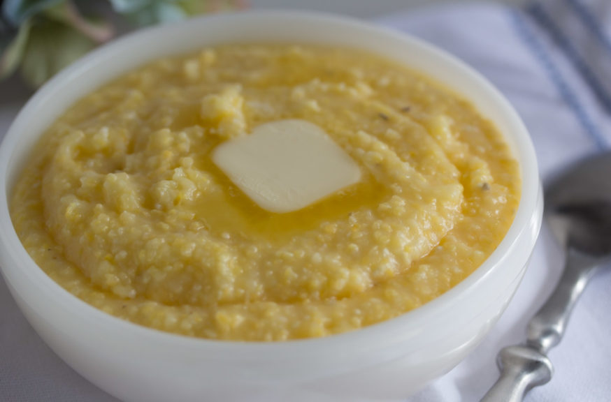 A bowl of creamy yellow grits with a pat of melting butter. 