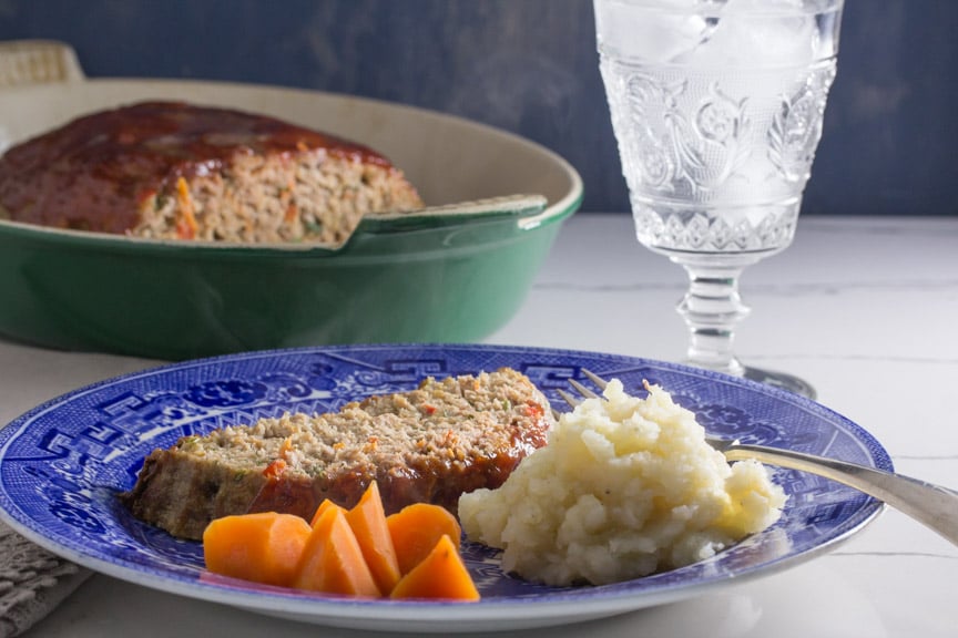 A slice of meatloaf served with mashed potatoes and carrots. 