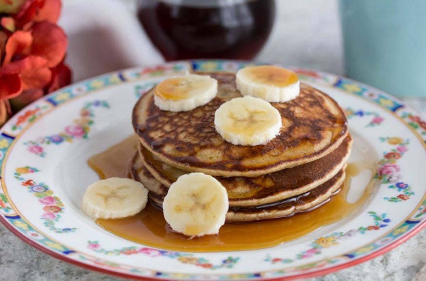 Sliced bananas with maple syrup poured over 3 stacked Quinoa Pancakes on a plate. 