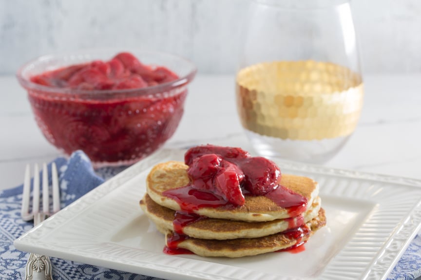 A stack of 3 fluffy protein packed Quinoa Pancakes topped with juice laden roasted strawberries. 