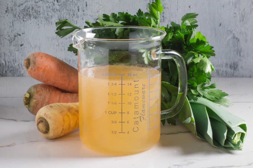 A glass measuring container filled with homemade Low FODMAP vegetable broth. 