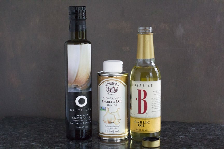 3 tall glass garlic oil bottles against a black background