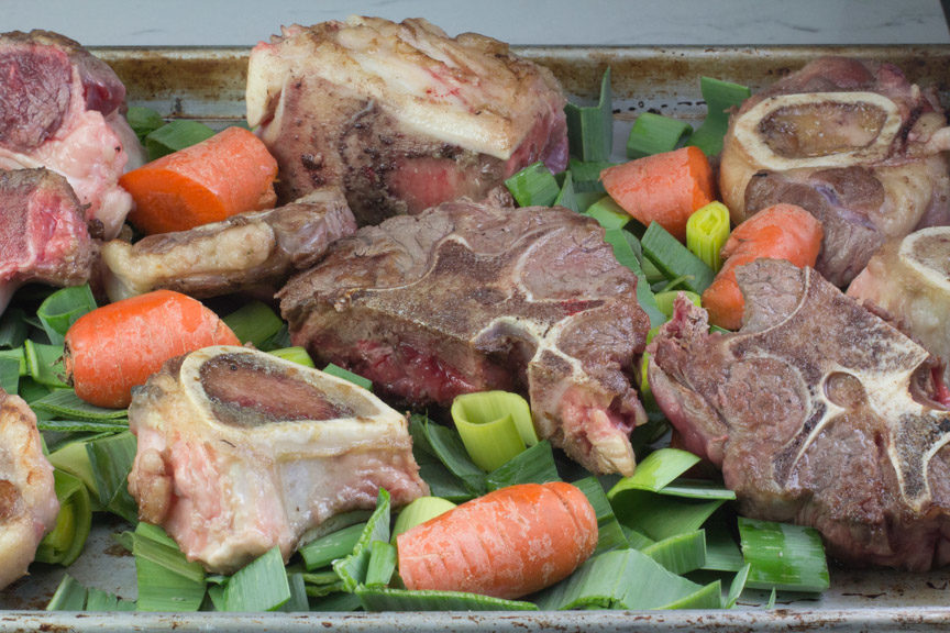 meaty bones, leek greens and carrots ready to roast for homemade low FODMAP Beef Stock