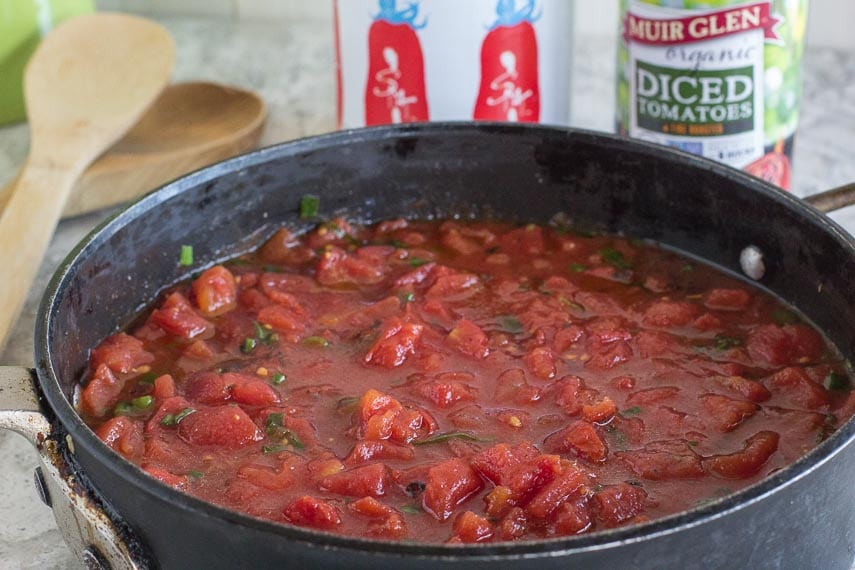 Super Simple Chunky Tomato Sauce in black saucepan, cans of tomatoes in background