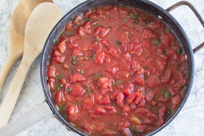 Super Simple Chunky Tomato Sauce in black saucepan, cans of tomatoes in background