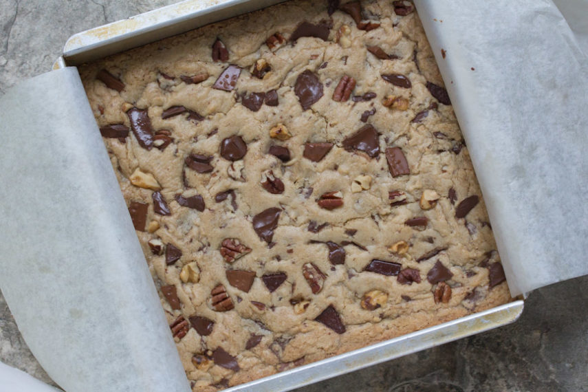 A top down view of a pan of just baked Low FODMAP chocolate chunk nut blondies - with lots of bigs chunks of chocolate