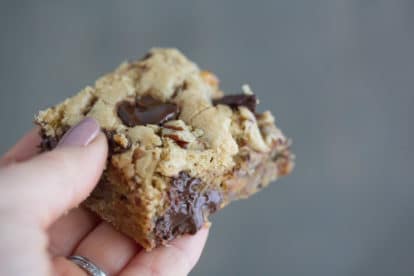 A hand offering a moist delicious chocolate chunk nut blondie.