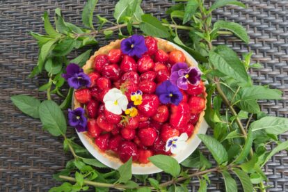 A vibrant fresh strawberry glazed tart, with pansies surrounded chocolate mint.