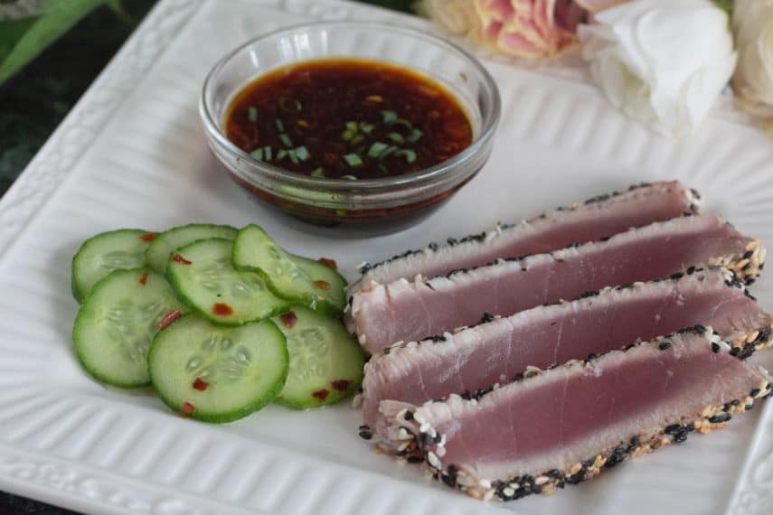Low FODMAP Sesame Crusted Tuna & pickled cucumbers sliced and laid out on a white square plate with dipping sauce. 