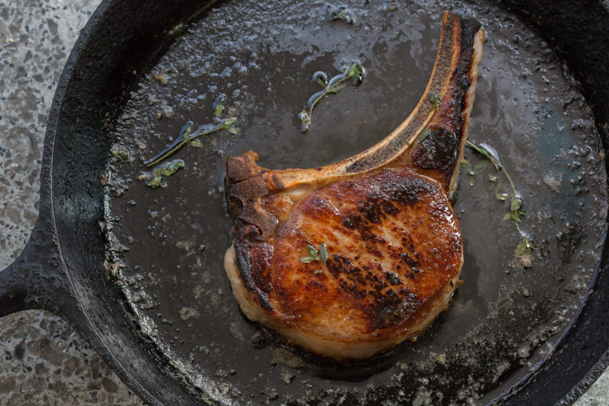 Pan Roasted Brined Pork Chop sizzling in a pan 