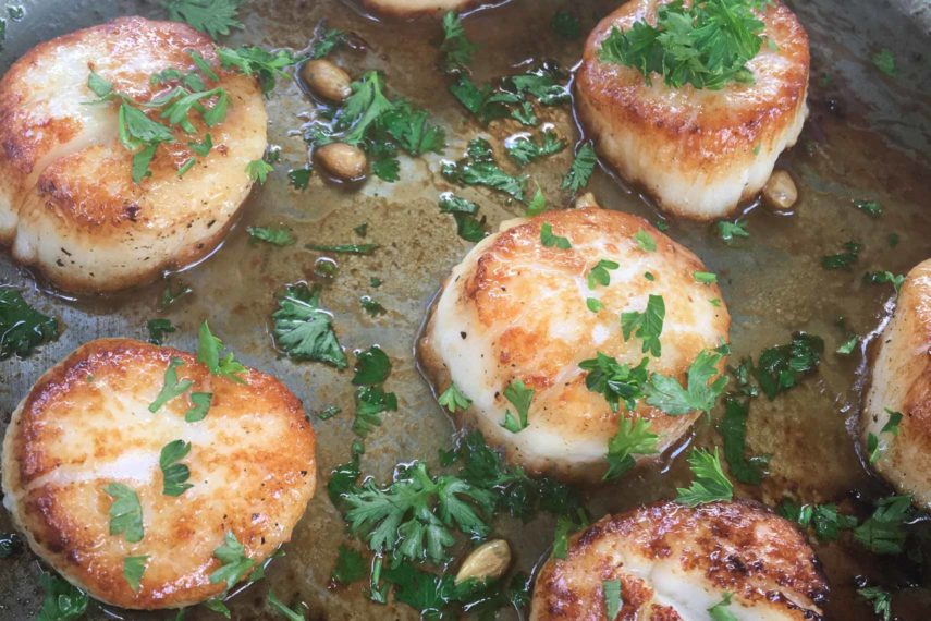 Caramelized juicy pan-seared scallops tossed in lemon and parsley in a pan. 