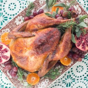 A gorgeously roasted Beer & Brown Sugar brined turkey seen from overhead - on a platter with pomegranates and oranges.