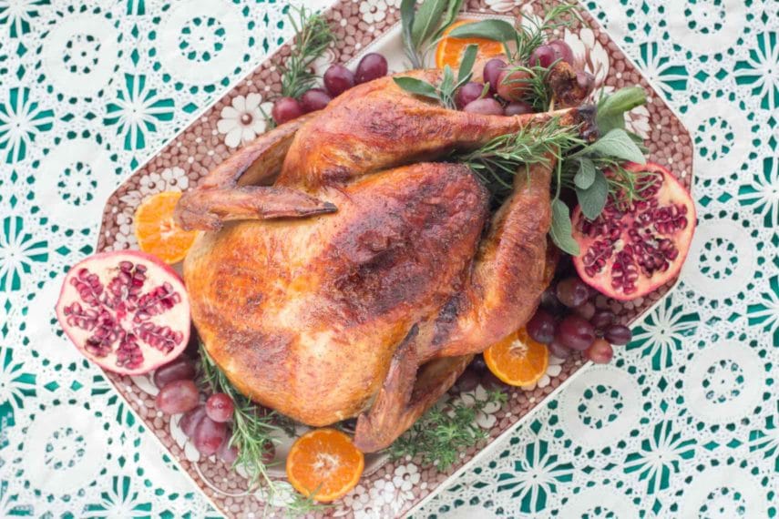 A gorgeously roasted Beer & Brown Sugar brined turkey seen from overhead - on a platter with pomegranates and oranges.