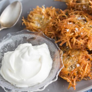 closeup shot of potato latke with flaked salt on a grey oval platter with lactose-free sour cream
