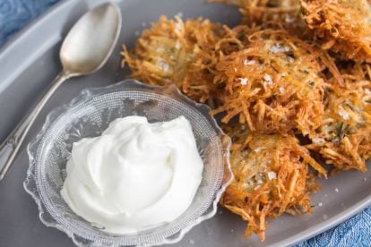 closeup shot of potato latke with flaked salt on a grey oval platter with lactose-free sour cream