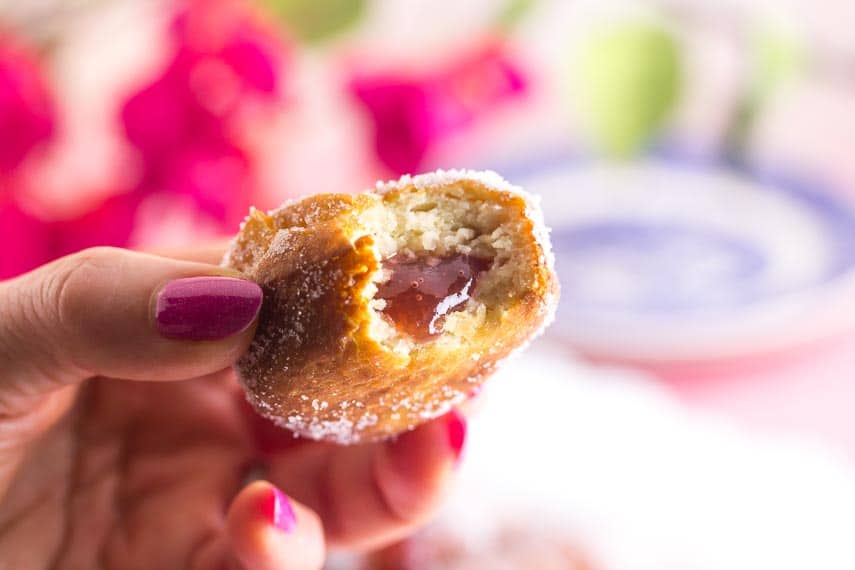 closeup of gluten-free jelly doughnut held in hand with pink nail polish