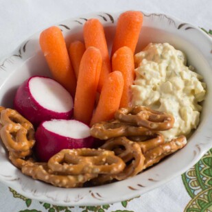 Egg salad with baby carrots, radishes and gluten free pretzels in an oval dish