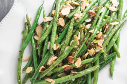 pan-roasted green beans topped with toasted almonds on an oval white platter