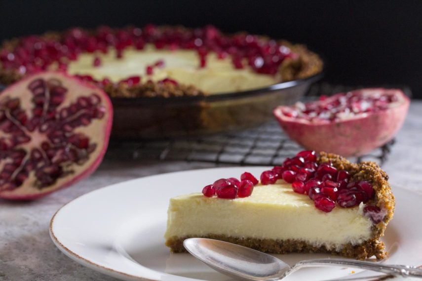 lactose-free cheesecake pie in a pat-in crust topped with pomegranate with whole pie in background and slice on a plate in the foreground