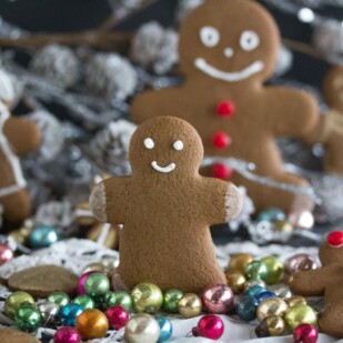 little gingerbread boy decorated with royal icing standing up amidst cookies and ornaments