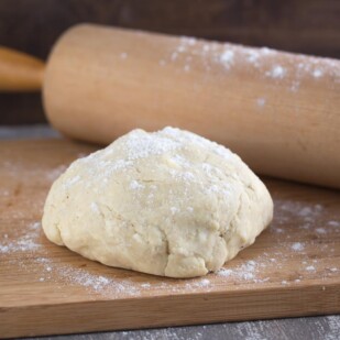 a ball of all butter pie crust with rolling pin on floured board