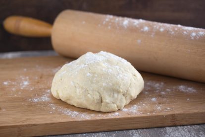 a ball of all butter pie crust with rolling pin on floured board