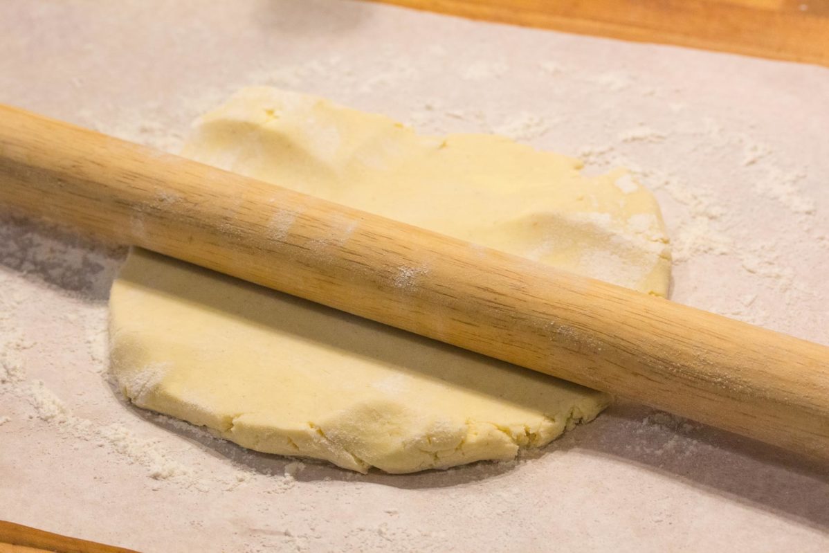 a rolling pin mid-roll with pastry dough on parchment paper