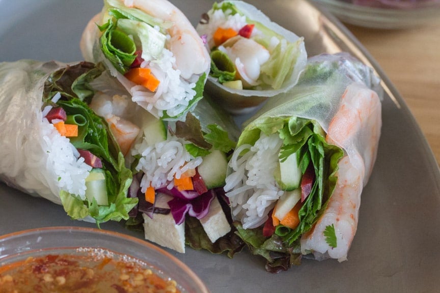 Summer Rolls cut open on a plate with a bowl of dipping sauce. 