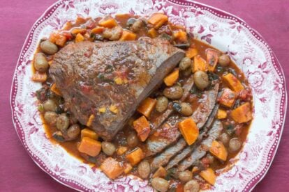 overhead image of brisket with sweet potatoes & grapes in a red and white platter