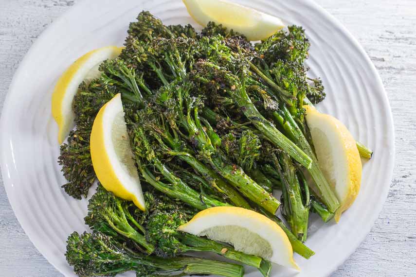Low FODMAP Spicy Roasted Broccolini with Garlic & Lemon on a round white plate and a white wood background
