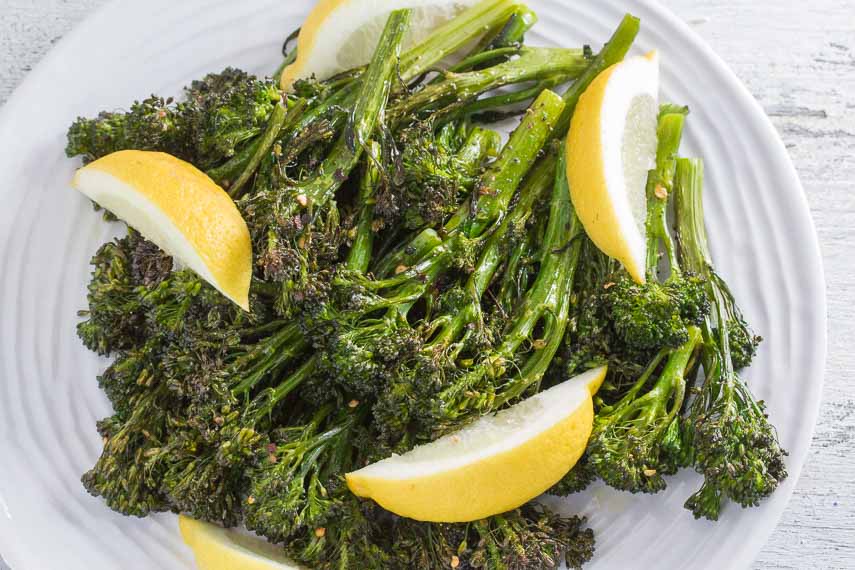 spicy roasted broccolini with garlic and lemon on a round white plate and a white wood background 