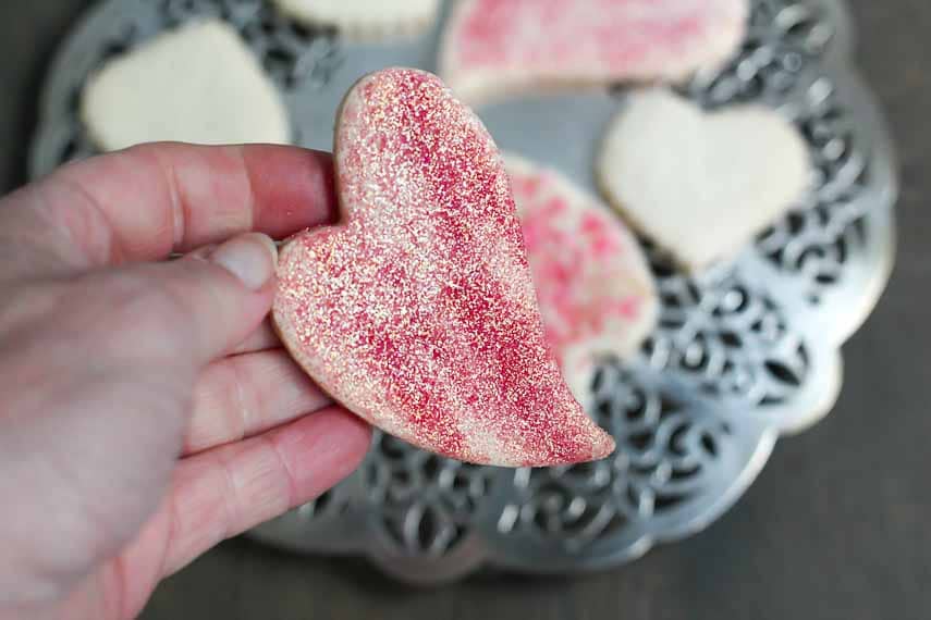 Low FODMAP, gluten-free Valentine's Day cookies, sprinkled with sparkly sugar, held in hand