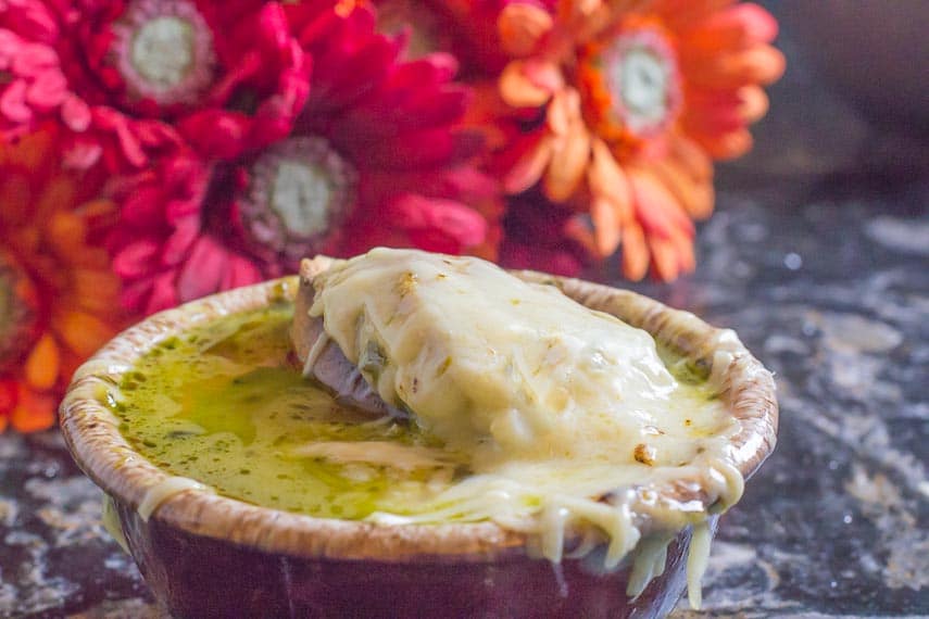 French onion soup in a brown bowl with melted cheese and red and orange flowers in the background