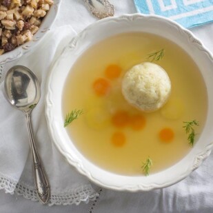 Matzo ball soup in a white bowl with charoset in the background