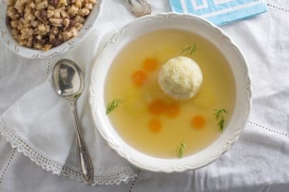 Matzo ball soup in a white bowl with charoset in the background