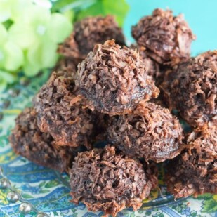 a mound of chocolate macaroons on a plate; aqua background and flowers on the side