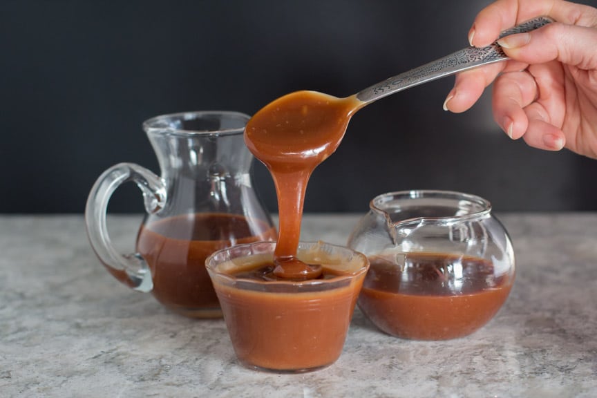 salted caramel sauce pouring from spoon against a black background