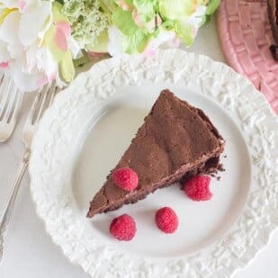 flourless chocolate cake on a white plate with fresh raspberries