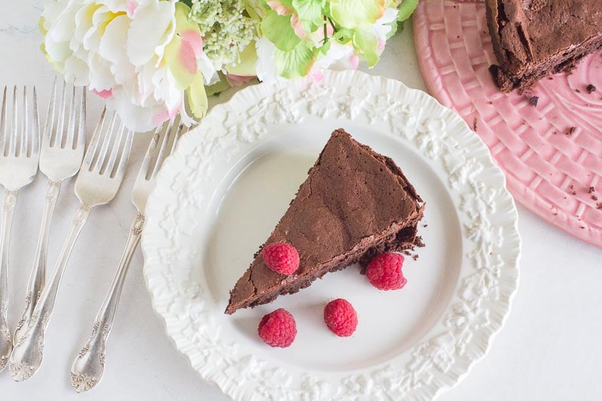 flourless chocolate cake on a white plate with fresh raspberries