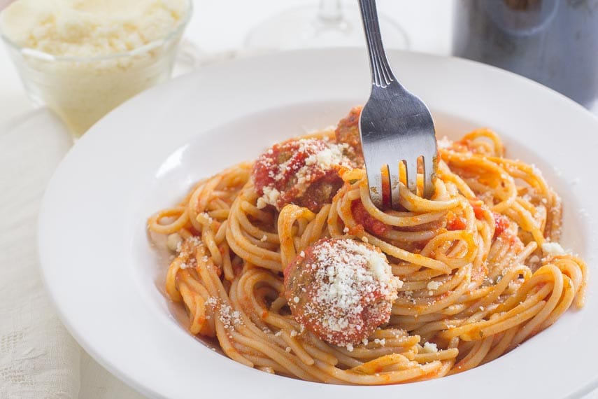 fork twirling in spaghetti & meatballs, in a white bowl