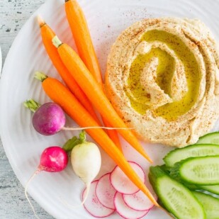 hummus on a white plate with low FODMAP vegetables and gluten-free pretzels