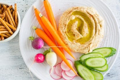 hummus on a white plate with low FODMAP vegetables and gluten-free pretzels