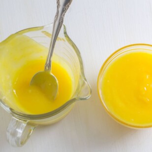 lemon curd in a glass cup; also in a measuring cup with spoon inserted