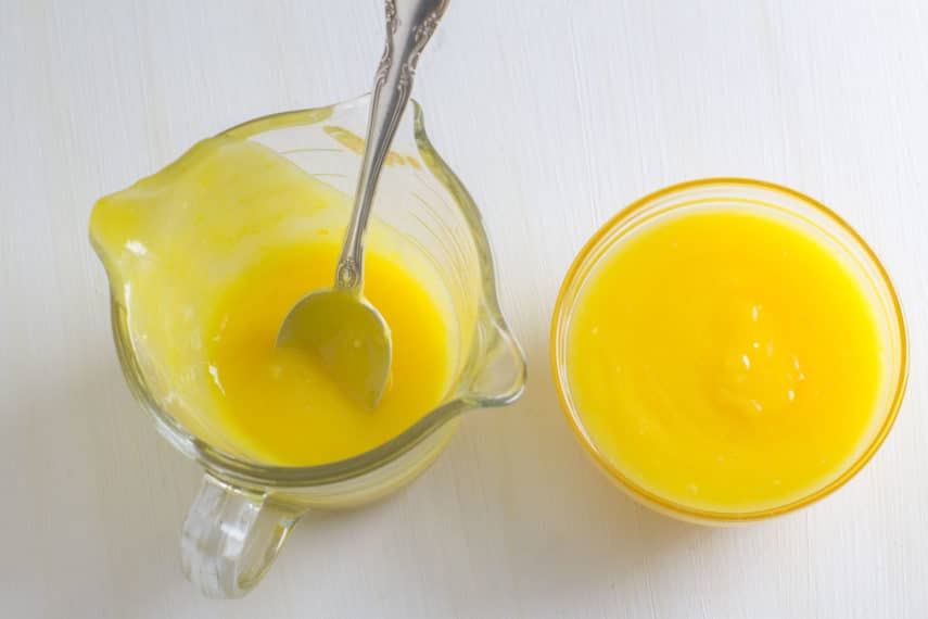 lemon curd in a glass cup; also in a measuring cup with spoon inserted 