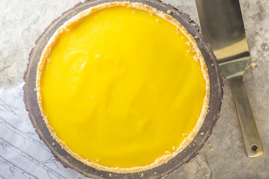 lemon curd tart in a shortbread crust on a stone background with a gold toned spatula