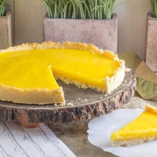 lemon curd tart on a wooden platter, a slice out on thew side on a white plate