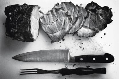 overhead black and white shot of sliced ham on a board with a carving knife and fork