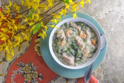 overhead shot of shrimp and chicken congee and greens in a bowl set on a stone background copy