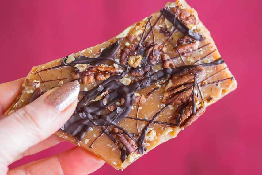pecan toffee closeup against red background, being held in hand